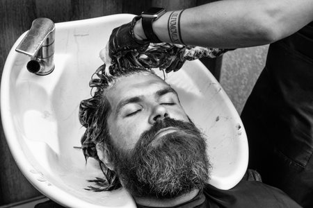 bearded man in hairdresser salon. beauty and fashion. hair and beard styling. confident brutal guy with barbershop professional master. hipster wash in washbasin. male barber care. Cosmetic for spaの写真素材