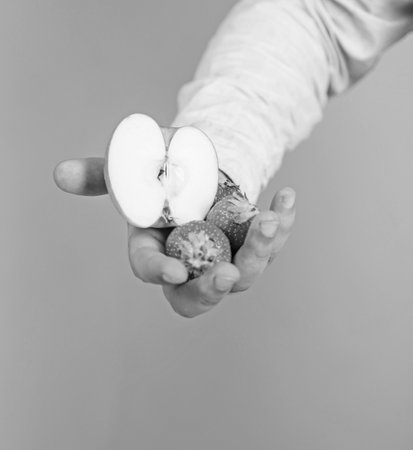 Male hand with strawberries and half of apple blue background. Help yourself. Hand proposes take strawberry and apple fruit. Fruits organic treat or snack. Fresh harvest of ripe fruit berriesの写真素材