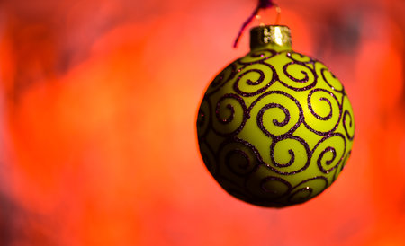 Festive decoration for Christmas tree, yellow ball with glitter decor, on red blurred background. Ornament concept. Christmas decoration or toy for Christmas tree with shimmering detailsの写真素材