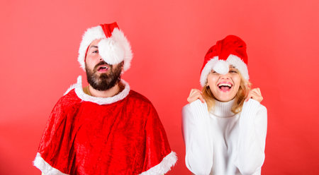 Christmas masquerade or karnival concept. Couple cheerful face celebrate christmas. Couple celebrate winter holiday christmas party. Man with beard and woman in santa hat with pompon red backgroundの写真素材