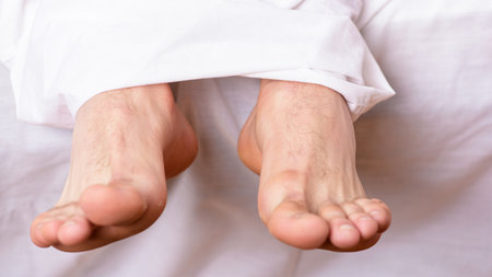 Man sleeping on bed under blanket. Sleep alone. Healthy skin on foot. Size of foot. Male feet on bed...