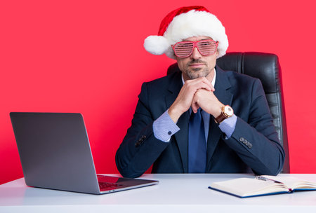 mature boss wear red santa claus hat and party glasses in business officeの写真素材