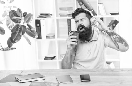 Happy man singing to takeaway cup listening to song in headphones in office, musicの写真素材