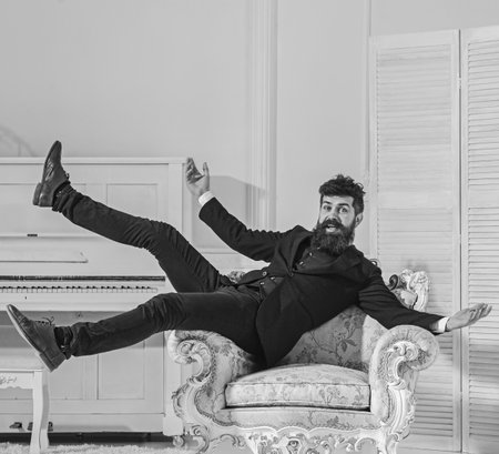 Man with beard and mustache wearing fashionable classic suit, sits, jumps on old fashioned armchair....