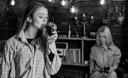 Friends enjoy mulled wine in warm atmosphere, wooden interior. Girls relaxing and drinking mulled wine. Rest and relax concept. Friends on relaxed faces in plaid clothes relaxing, defocusedの写真素材