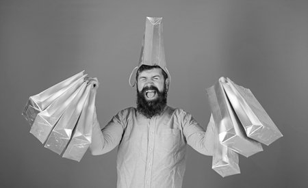 Man with trendy beard wearing pink shirt and silver bag on his head isolated on blue background. Shopping champion winning first prize in contest, happiness concept. Bearded man enjoying sales timeの写真素材