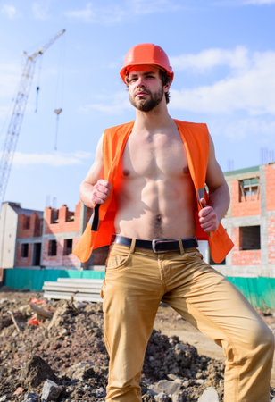 Builder sexy muscular torso macho dream of every woman. Sexy macho foreman. Builder orange vest helmet work construction site. Guy protective helmet stand in front of building made out of red bricksの写真素材