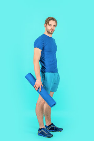 sport man with fitness yoga mat isolated on blue background. sport man with yoga mat