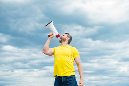 man in yellow shirt shout in megaphone on sky background. communicationの写真素材