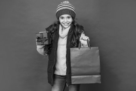 happy child in winter clothes hold shopping bag and box on red background, purchaseの写真素材