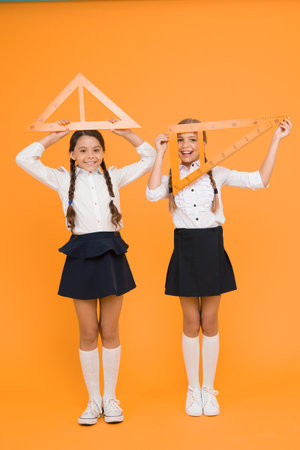 bright minds. Kids in uniform at yellow wall. friendship and sisterhood. happy small girls study mathematics. students use gon ruler. stem disciplines. back to school. Maths and geometryの写真素材
