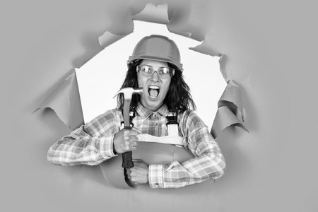 repair and renovation. woman wear protective glasses helmet. girl builder in hard hat on construction site. engineer hold hammer. young female worker on blue backgroundの写真素材