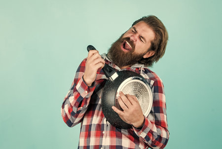mature handsome man in checkered shirt hold pan for cooking food, kitchen