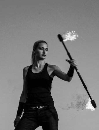 Sensual woman fire manipulator perform flaming baton twirling evening blue sky outdoors, dangerous