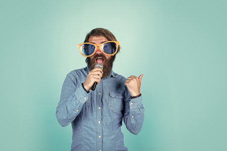making your party funny. brutal caucasian hipster event manager. funny party glasses. karaoke and music. male speaker with mic. vocal. happy smiling mature man. guy with beard sing in microphoneの写真素材