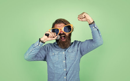 Music is an outburst of the soul. mature bearded man in funny party glasses sing song. brutal male hipster with microphone. vocal school. favorite music style. performer having funの写真素材