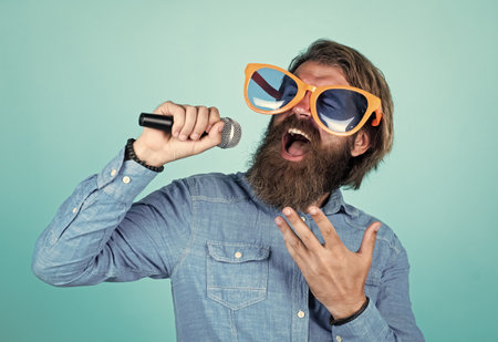 love is the music. male singer singing song in microphone. celebrate the anniversary. party goer. hipster man with beard wearing glasses. music concept. have a happy holiday. have fun on partyの写真素材