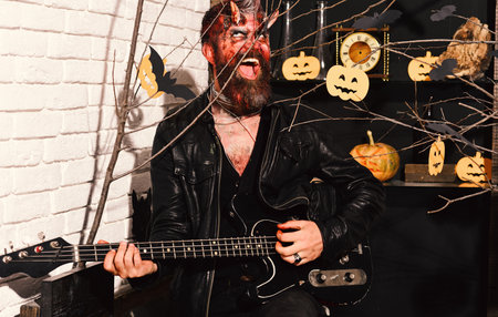 Devil or monster playing instrument. Demon with horns and mad smile holds black electric guitarの写真素材