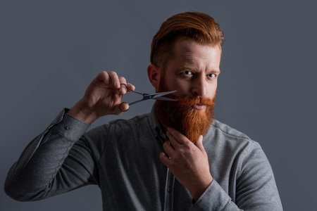 unshaven man barber hairdressing isolated on grey. man hairdressing with barber scissors.の写真素材