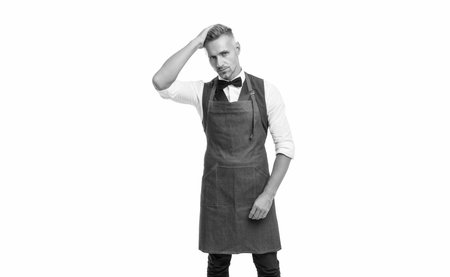 Serious man in bow and bartender apron fixing hair isolated on white, barkeeperの写真素材