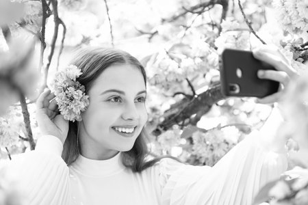 Portrait of happy girl taking selfie at flowering sakura tree in springの写真素材
