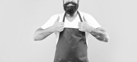 Happy man in red apron giving double thumbs yellow background, household serviceの写真素材