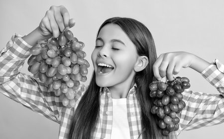 happy teen girl with grapes bunch on yellow background