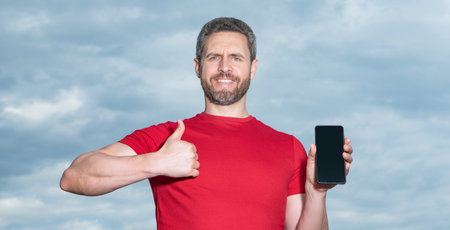 man showing phone app on sky background, thumb up. man showing phone app outdoor.の写真素材