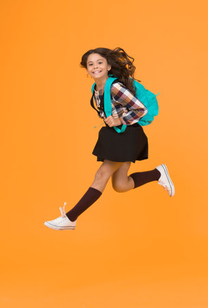Moving with haste. Energetic child in midair yellow background. School girl in energetic jump. Back to school fashion. School essentials. Energetic mood. Healthy and energeticの写真素材