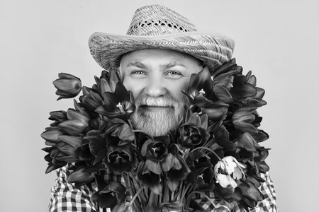 cheerful old retired man portrait in hat hold spring tulip flowers on green backgroundの写真素材