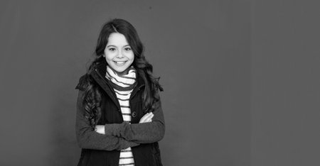 cheerful kid with curly hair in puffer waistcoat. teen girl on red background.