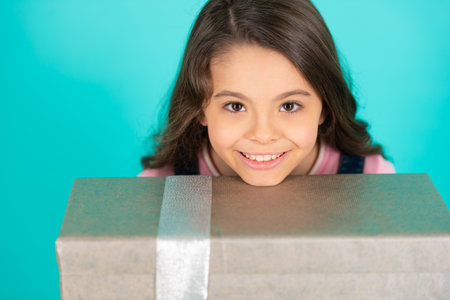 cheerful girl with birthday gift isolated on blue. girl with birthday gift in studio.の写真素材