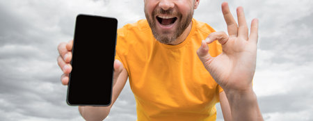 cropped view of guy presenting smartphone screen with copy space. showing ok gesture