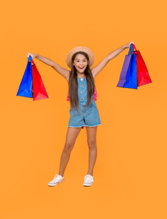 amazed teen child with shopping bags on yellow background. full length
