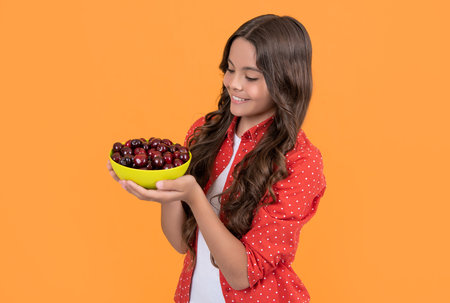 smiling teen girl hold cherry bowl on yellow backgroundの写真素材