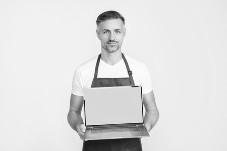 smiling mature man in apron presenting laptop with copy spaceの写真素材