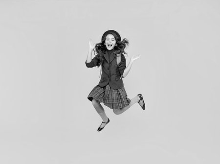 glad teen girl in uniform and beret with school bag running on yellow background, schoolgirlの写真素材