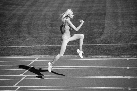 fit lady in fitness wear running on stadium racetrack while sport workout, speedの写真素材