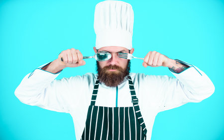 Time to try taste. Chef serious strict face hold spoon and fork. Man handsome with beard holds kitchenware on blue background. Cooking process concept. Lets try dish. Hungry chef ready to try foodの写真素材