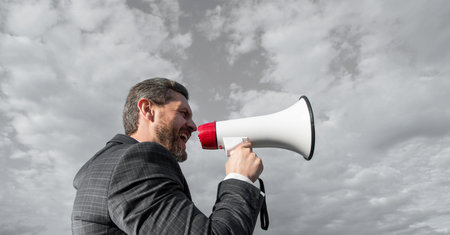 businessman shout in loud hailer on sky backgroundの写真素材