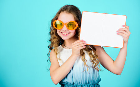Popular vacation books. Great books for summer vacation. Girl in sunglasses hold book. Summertime concept. Hobby and leisure. Top funny books to read. Beach reads for summer. Kid likes reading bookの写真素材