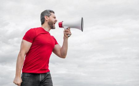 man in red shirt shouting in loudspeaker on sky backgroundの写真素材