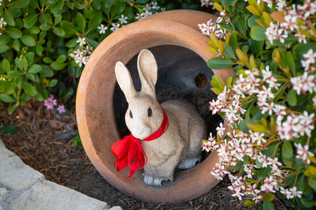 Rabbit figurine in garden pot. Rabbit sculpture in garden. White rabbit statue with red bowの写真素材