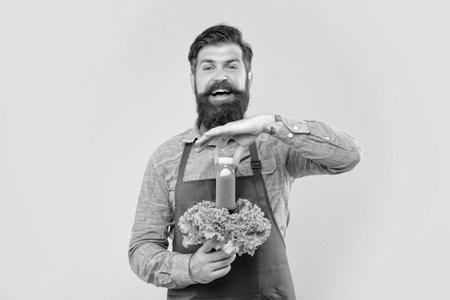 Happy man in apron holding fresh leaf lettuce holding juice bottle yellow background, juice barman.の写真素材