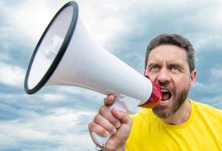 man in yellow shirt shout in loudspeaker on sky background. voice conceptの写真素材
