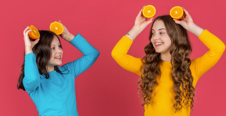 glad teen girls hold orange fruit on pink background