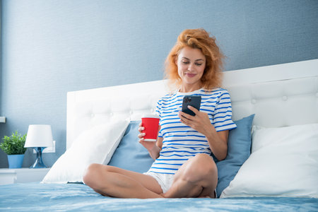 positive woman with coffee surfing internet on phone. woman surfing internet at home with phone.の写真素材