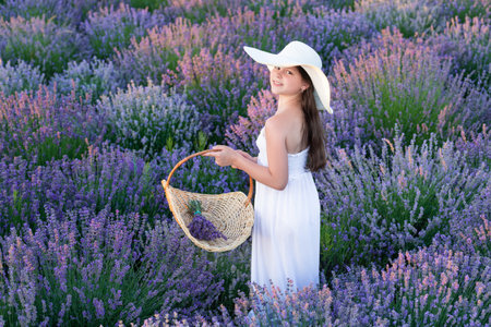 Teen girl in a dress walking in lavender park. glad teen girl with lavender in field. Teen girl with lavender flower standing in the field. teen girl with lavender holding a flower bouquetの写真素材