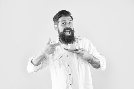 amazed mature hipster with beard pointing finger on coffee cup on yellow background, cappuccino.の写真素材