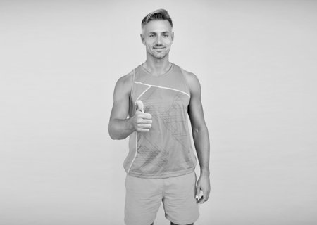 Happy sportsman blue background. Sportsman giving thumb gesture. Fit man in sportswear, sportsman.の写真素材